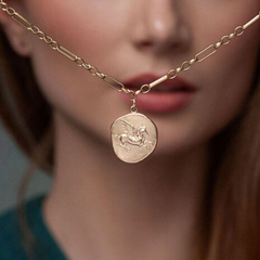 Gold necklace with a pegasus corinthian coin pendant held in front of models face