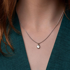 Necklace with a tiny pebble pendant worn by a person against a teal background