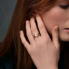 Close-up of a woman's hand wearing a rose gold ring with an ethically sourced gem stone, she is touching her hair.
