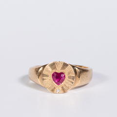 Gold ring with a heart-shaped ruby stone on a light gray background