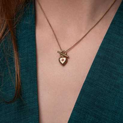 Gold necklace with a heart-shaped pendant worn by a person in a teal outfit.