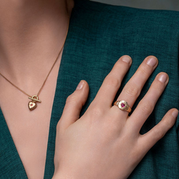 Gold necklace with heart pendant and ring with red gemstone on a teal fabric background