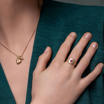 Gold necklace with heart pendant and ring with red gemstone on a teal fabric background